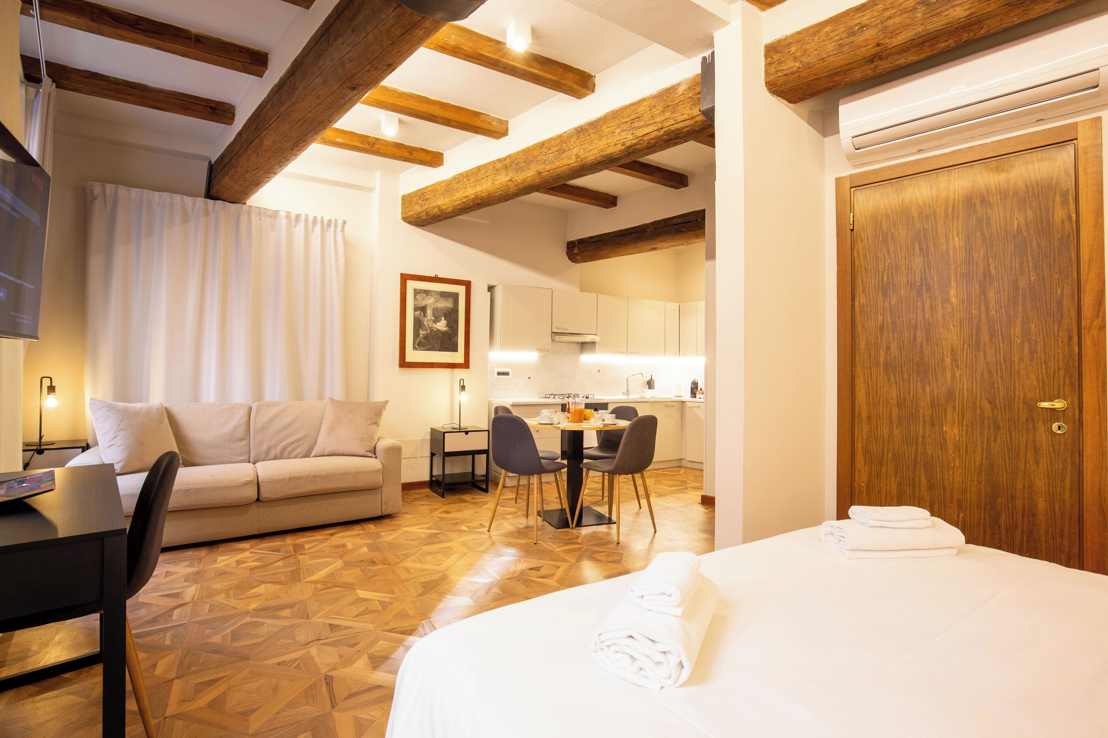 Une chambre d’hôtel comprenant un lit, un canapé, une table à manger avec des chaises, un coin cuisine et des poutres en bois au plafond.