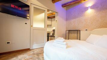 A hotel room with a bed, a flat-screen TV mounted on the wall, a wooden ceiling, and a patterned wall.