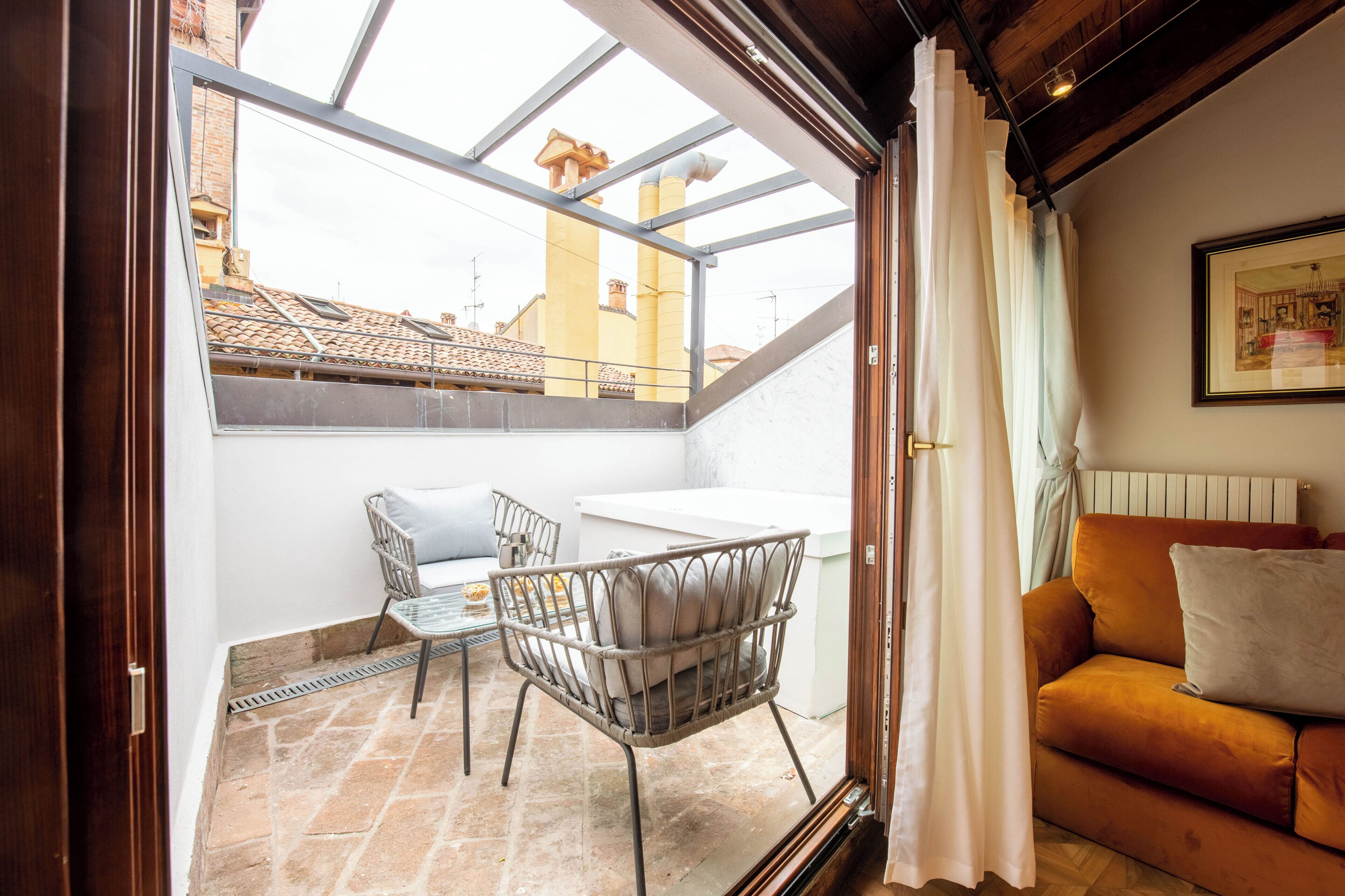 A balcony with a table and chairs, a sofa, and a view of buildings through a skylight.