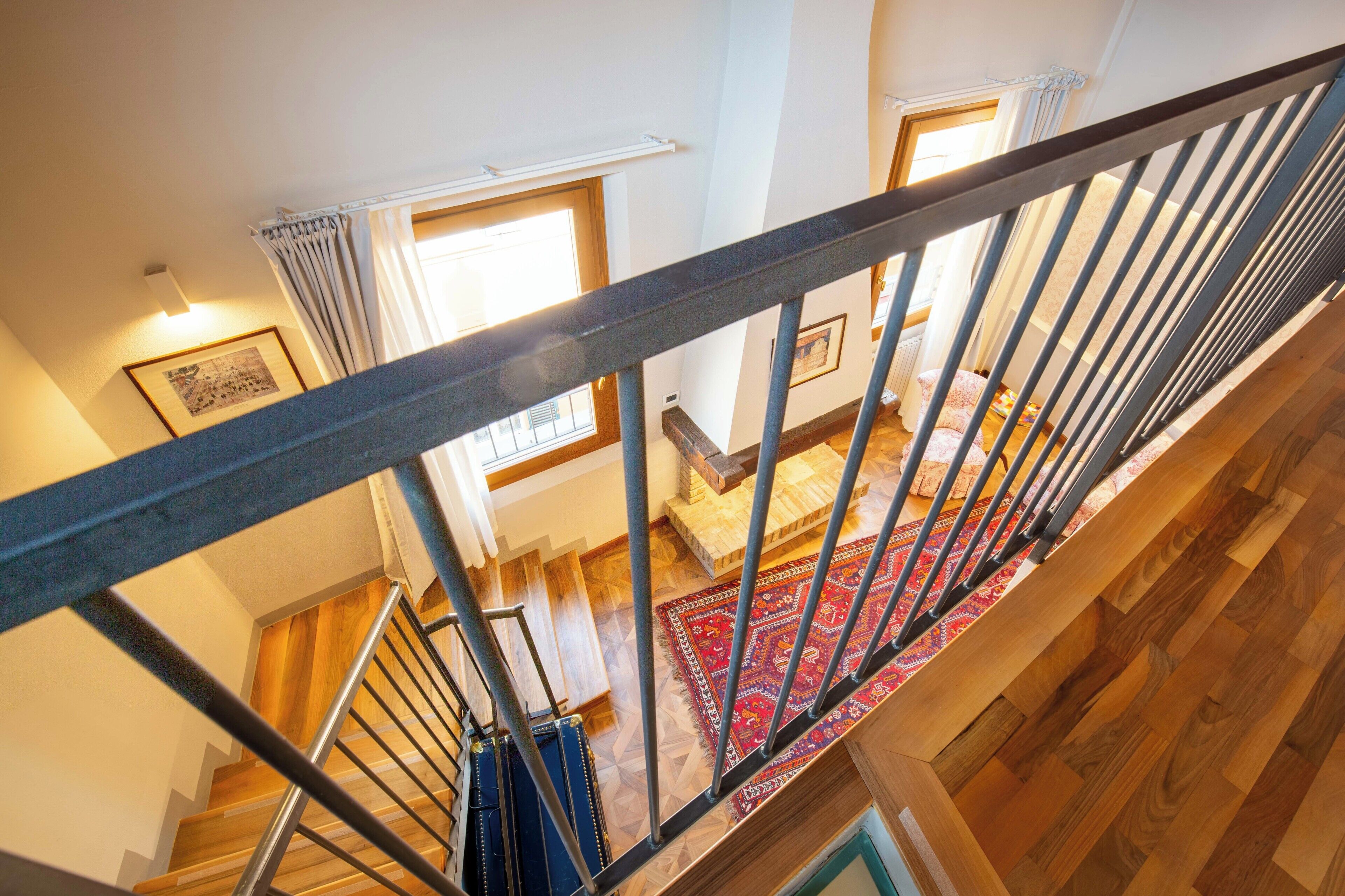 A staircase with wooden steps and metal railings, leading to a room with a red patterned rug and a bed with pillows.