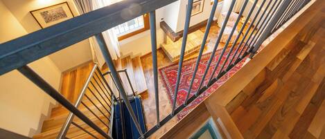 A staircase with wooden steps and metal railings, leading to a room with a red patterned rug and a bed with pillows.
