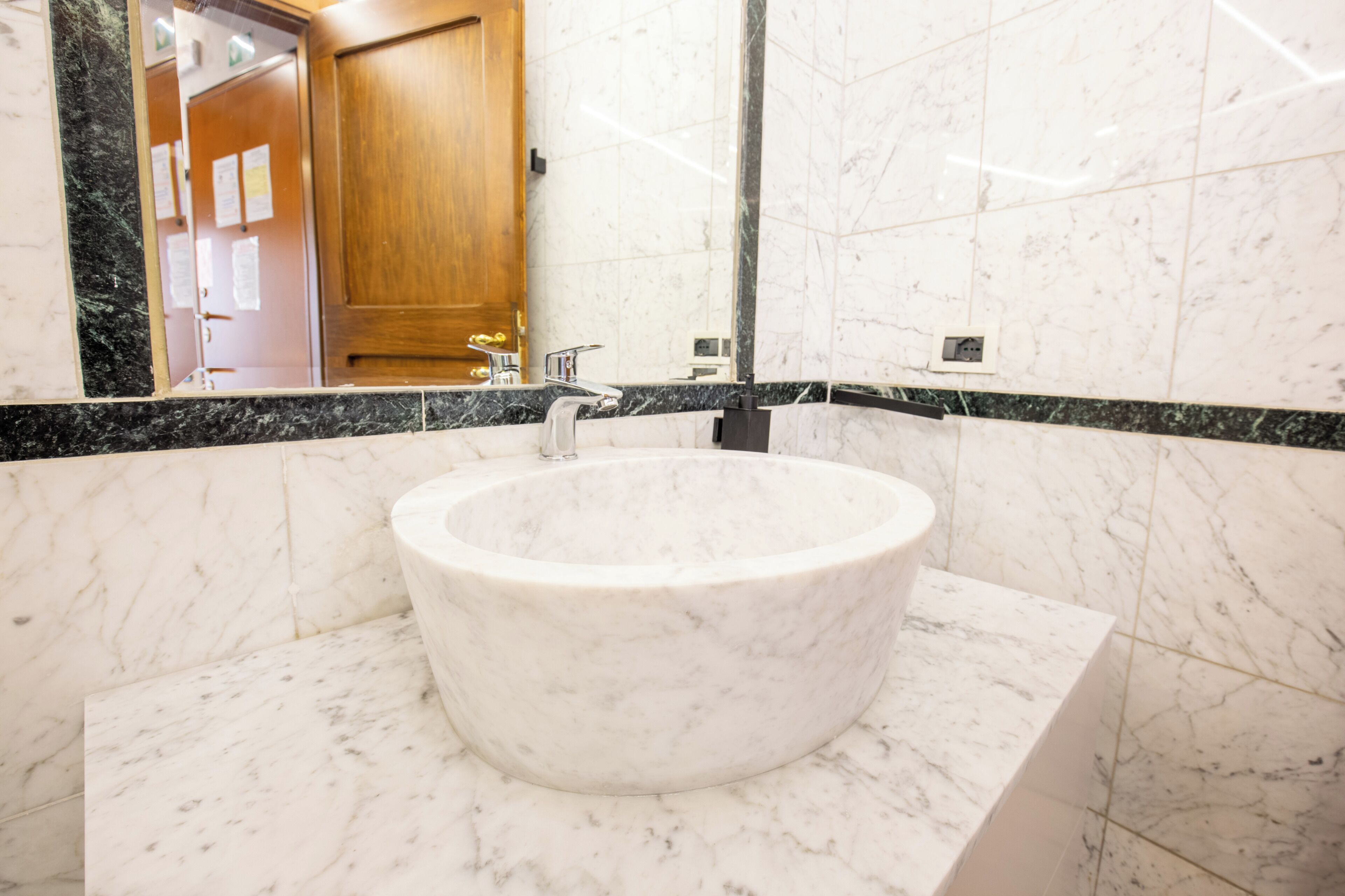 A bathroom with a marble sink, a wooden door, and a mirror.