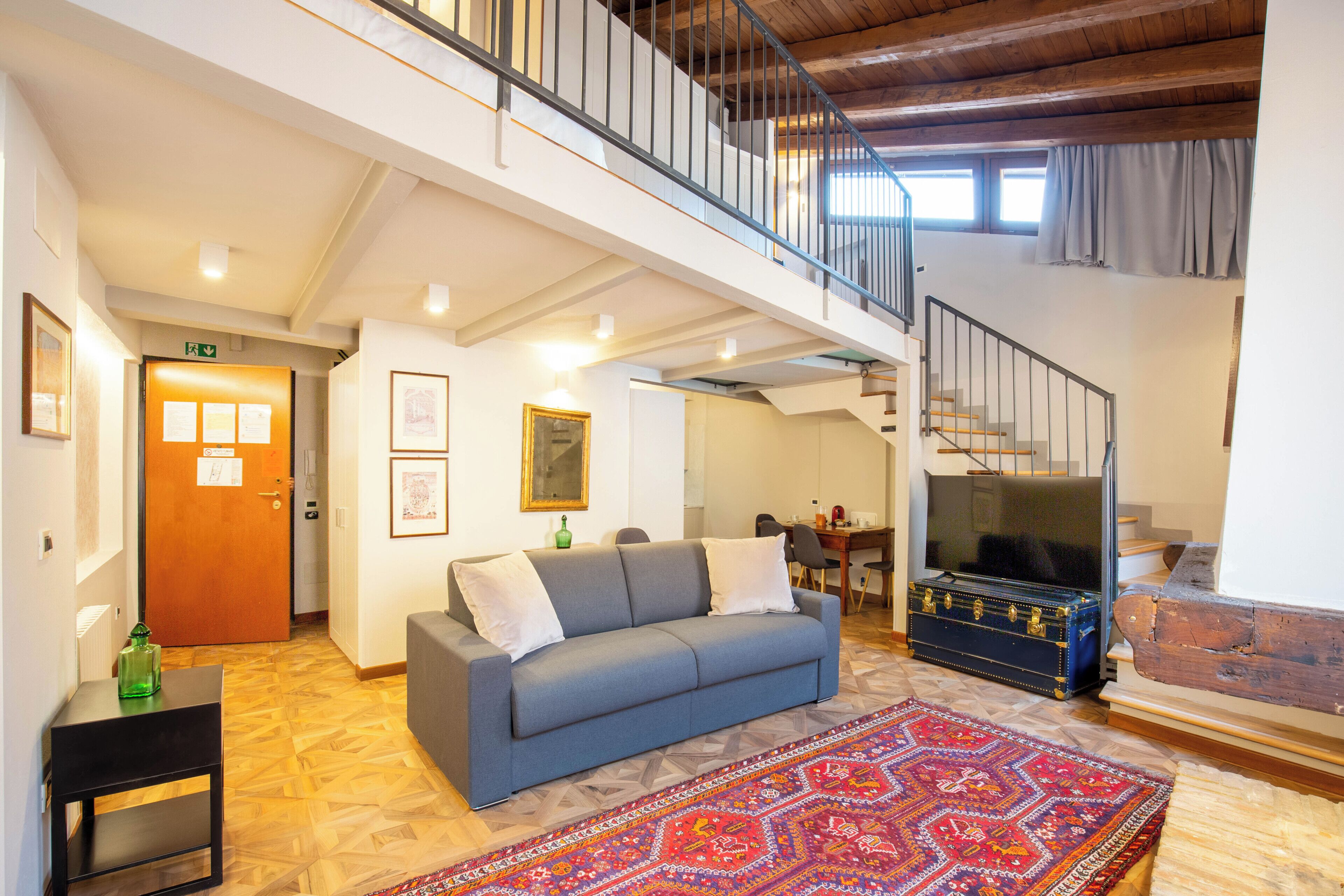 Uma sala de estar ampla com sofá, tapete estampado e escada de madeira.