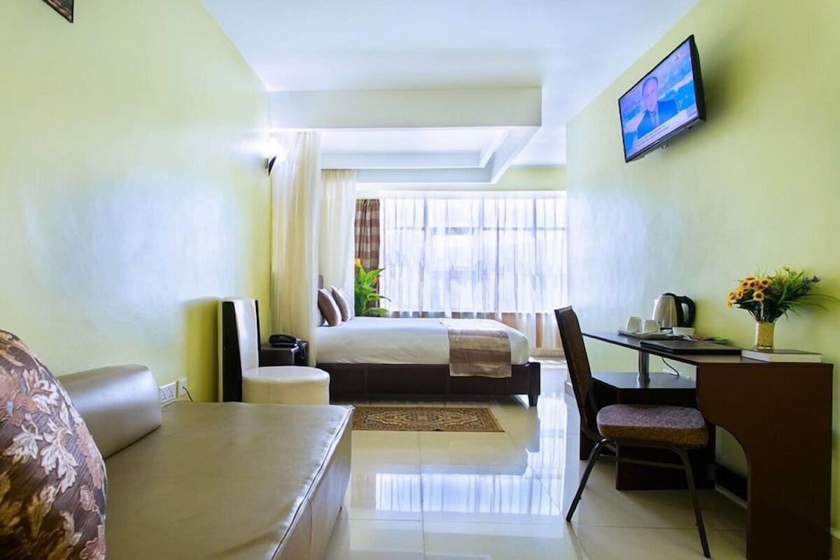 Habitación de hotel con cama, escritorio, silla, sofá, televisión y ventana con cortinas.