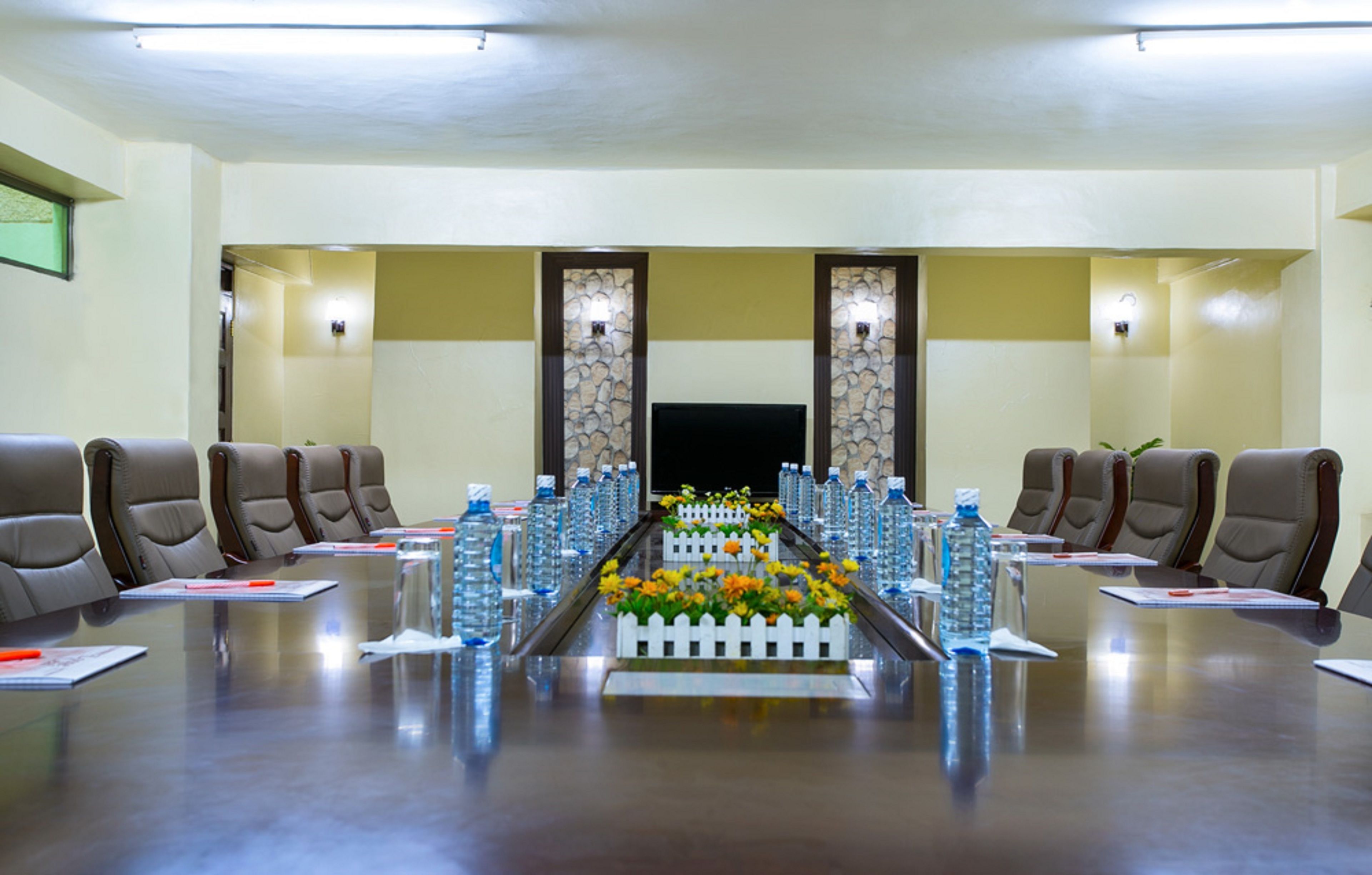 A conference room with a long table, chairs, water bottles, and a flower arrangement.