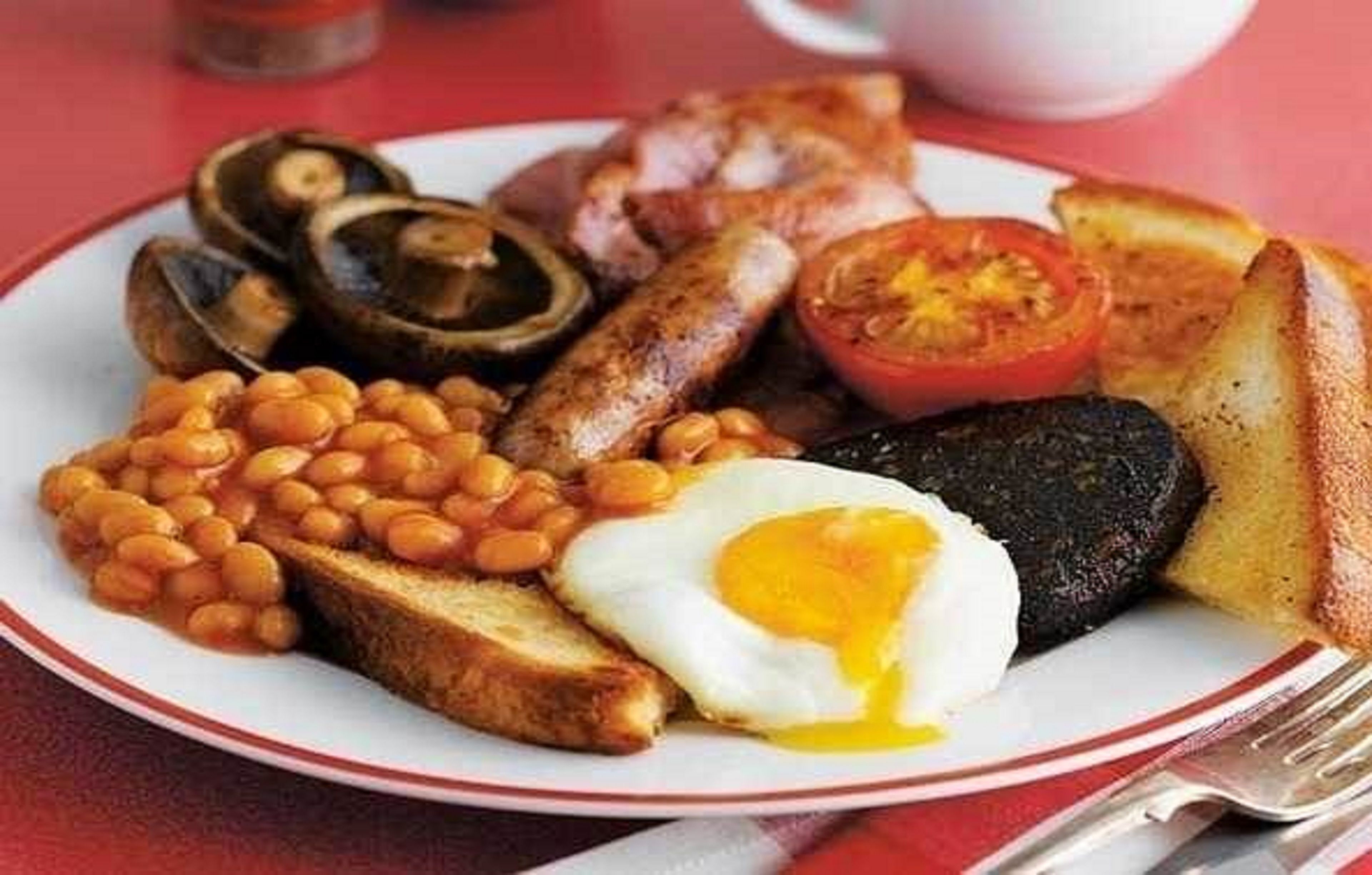 Ein Teller Frühstück mit Eiern, Würstchen, Pilzen, Bohnen, Toast und einer Tomate.