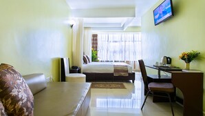 Una habitación de hotel con una cama, un escritorio, una silla, un televisor y un ventanal con cortinas.
