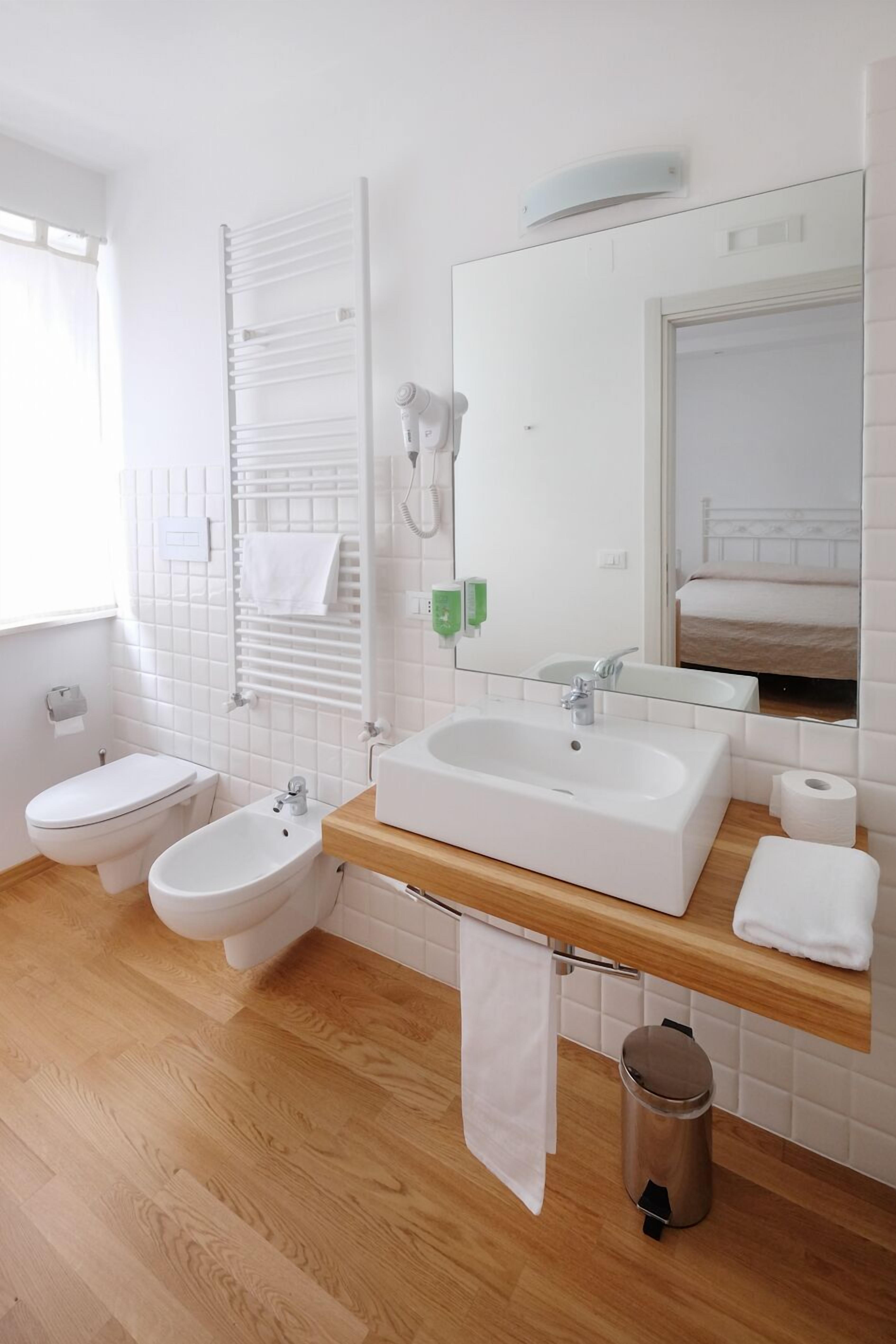 A modern bathroom with a wooden vanity, a large mirror, a toilet, and a bidet.