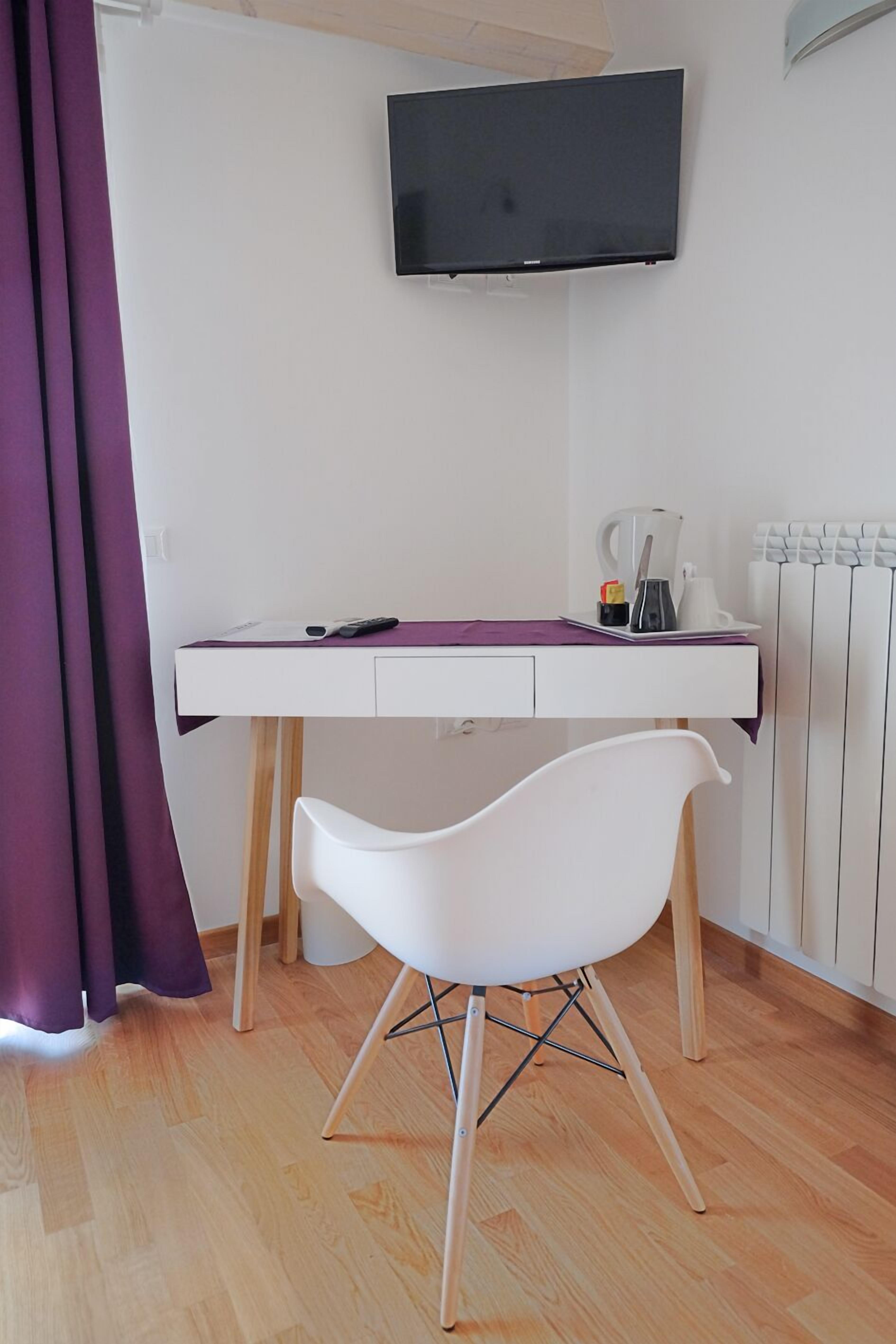 A modern room with a white desk, a white chair, a flat-screen TV mounted above the desk, and a radiator on the wall.
