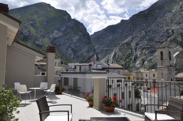 A terrace with white chairs and tables, overlooking a mountainous landscape with buildings and a tower. - Da Oreste Affittacamere (Fara San Martino)