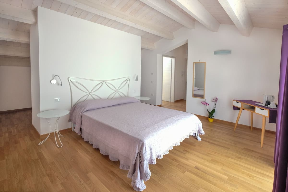 A bedroom with a bed, a small table, a chair, a mirror, and a desk with a lamp.
