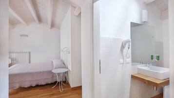 Ein Schlafzimmer mit Bett, kleinem Tisch und Stuhl. Der Raum hat Holzboden und weiße Wände.