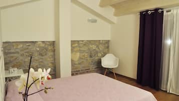 Una camera da letto con parete in pietra, un letto con copripiumino rosa, una sedia bianca e una finestra con tende scure.