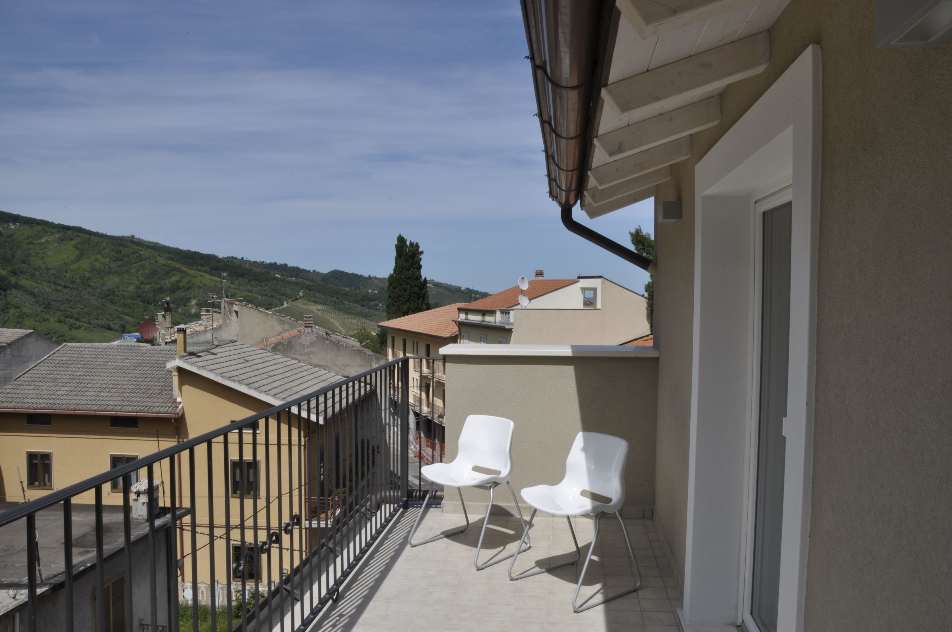 Un balcone con due sedie bianche, vista sugli edifici circostanti e cielo sereno.