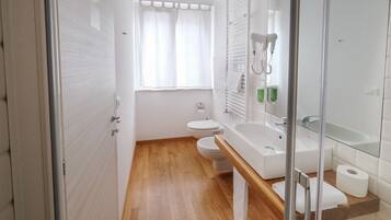 Un baño moderno con suelo de madera, sanitarios blancos, cabina de ducha de cristal y un espejo grande.