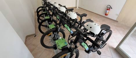 Une rangée de vélos, chacun équipé d’un casque et d’une étiquette verte, une porte blanche et un extincteur accroché au mur.