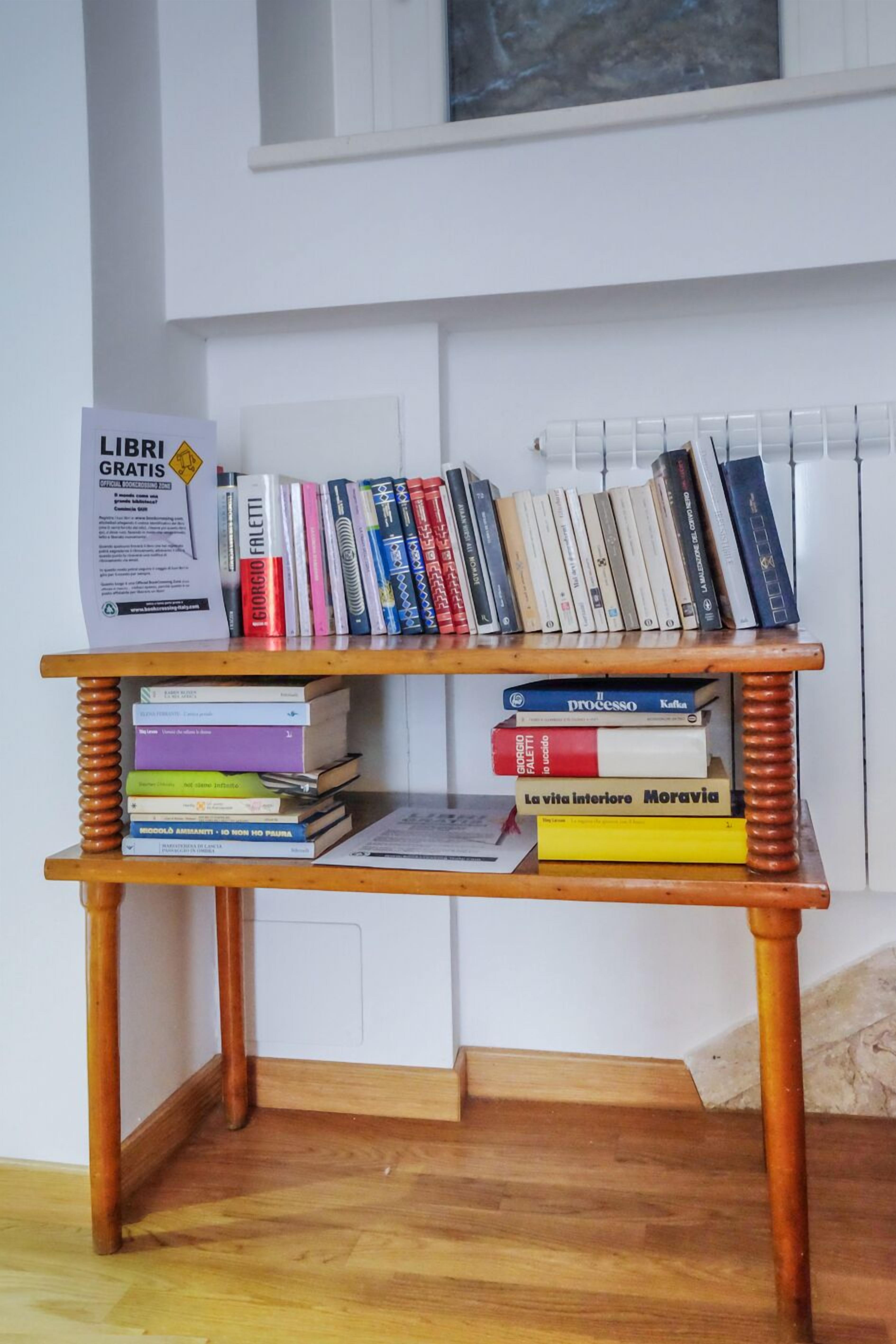 Ein Bücherregal aus Holz mit zahlreichen Büchern und einem Schild mit der Aufschrift 'LIBRI GRATIS'.