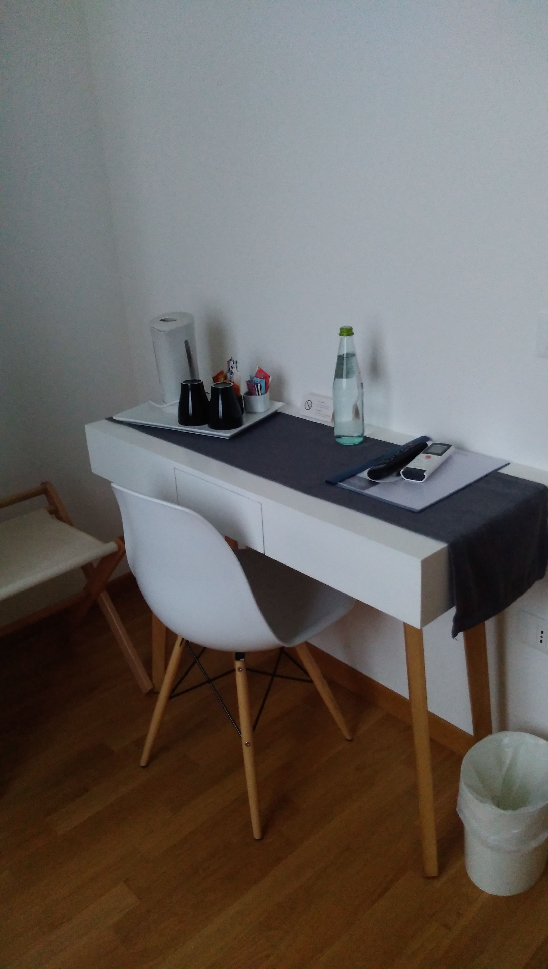 A small, white desk with a chair, a water bottle, a mobile phone, and a roll of paper towels.