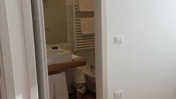 Een slaapkamer met een houten vloer, een bed, een aan de muur bevestigde televisie en een badkamer zichtbaar door een geopende deur.