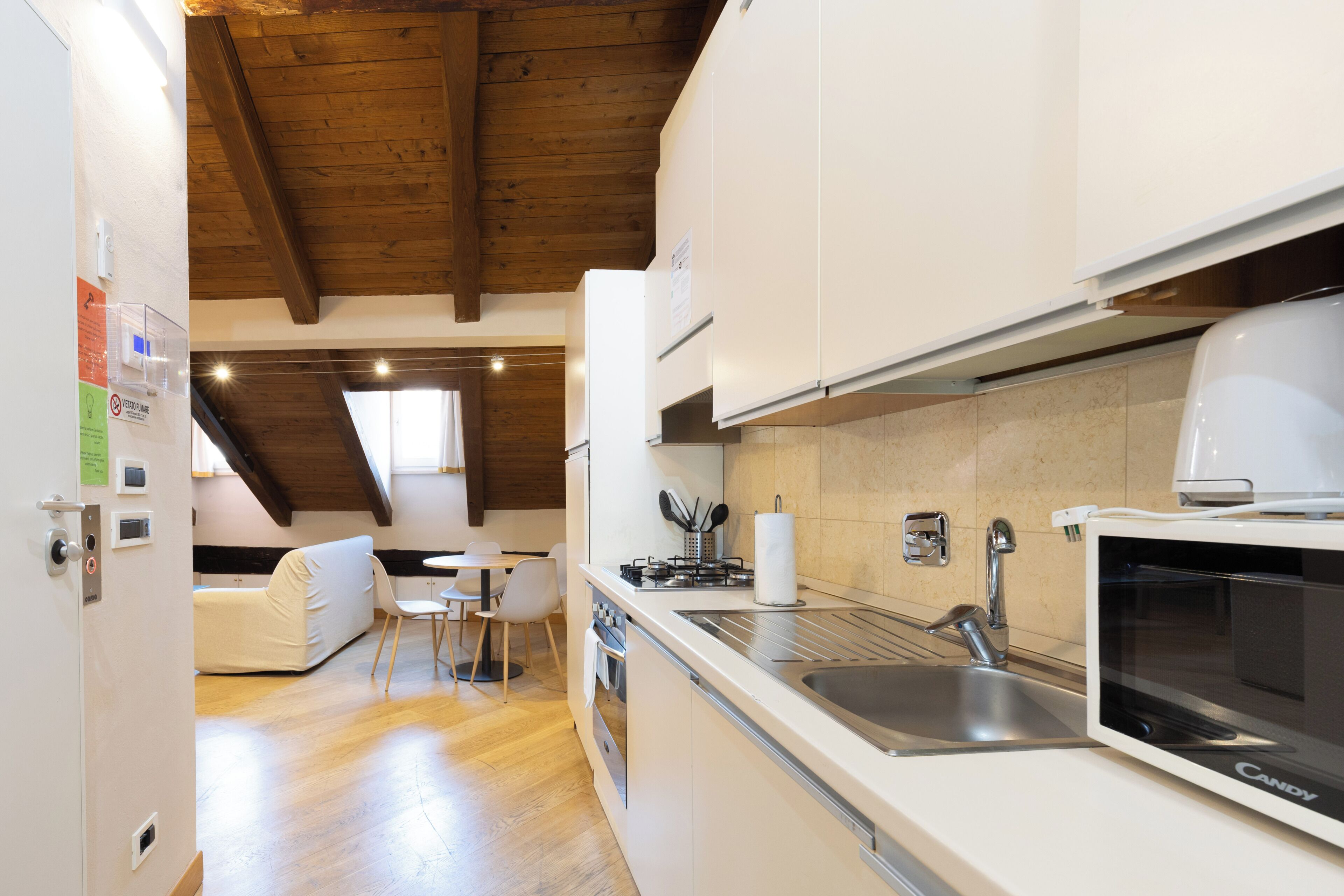 A modern kitchen with white cabinets, a built-in oven, a microwave, and a sink. There is a dining area with a table and chairs.