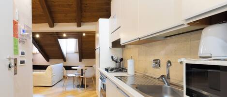 A modern kitchen with white cabinets, a built-in oven, a microwave, and a sink. There is a dining area with a table and chairs.