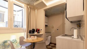 A compact kitchen with a sink, a coffee machine, and a toaster. There is a dining area with a table and chairs.