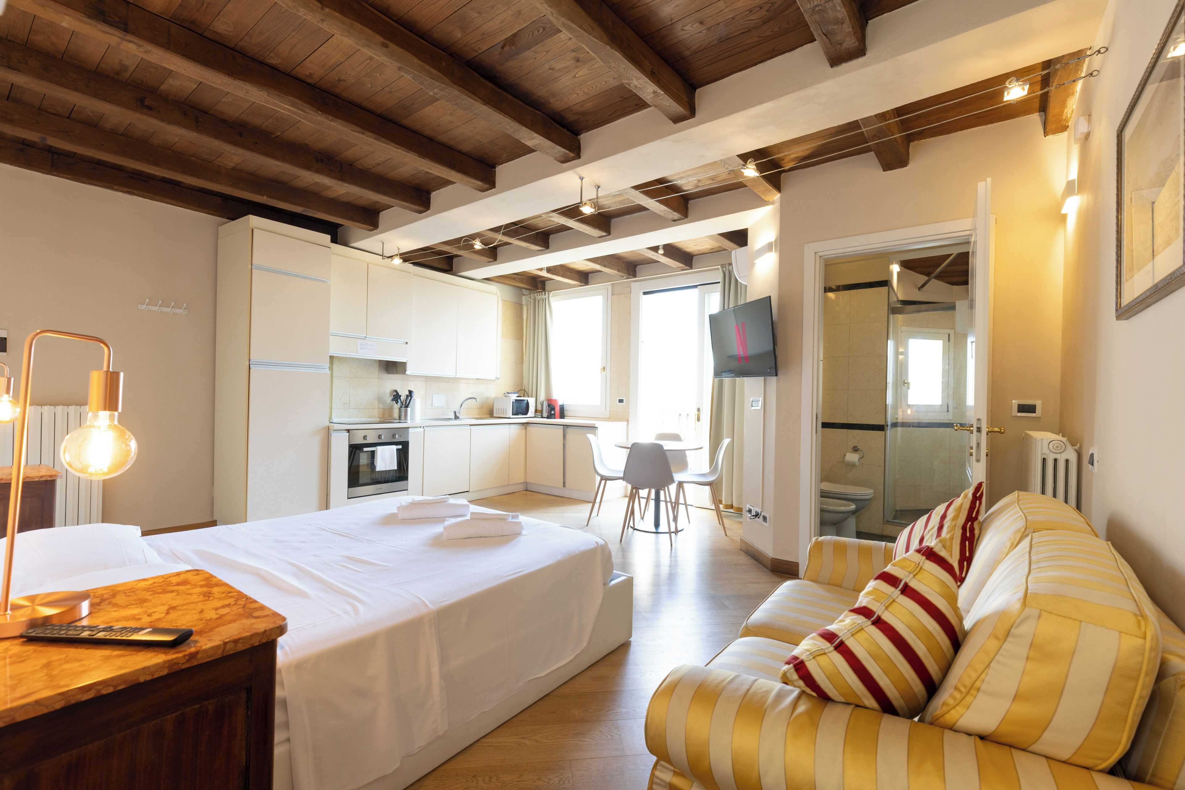 Una habitación de hotel con cama, sofá, escritorio con lámpara, televisor y kitchenette.
