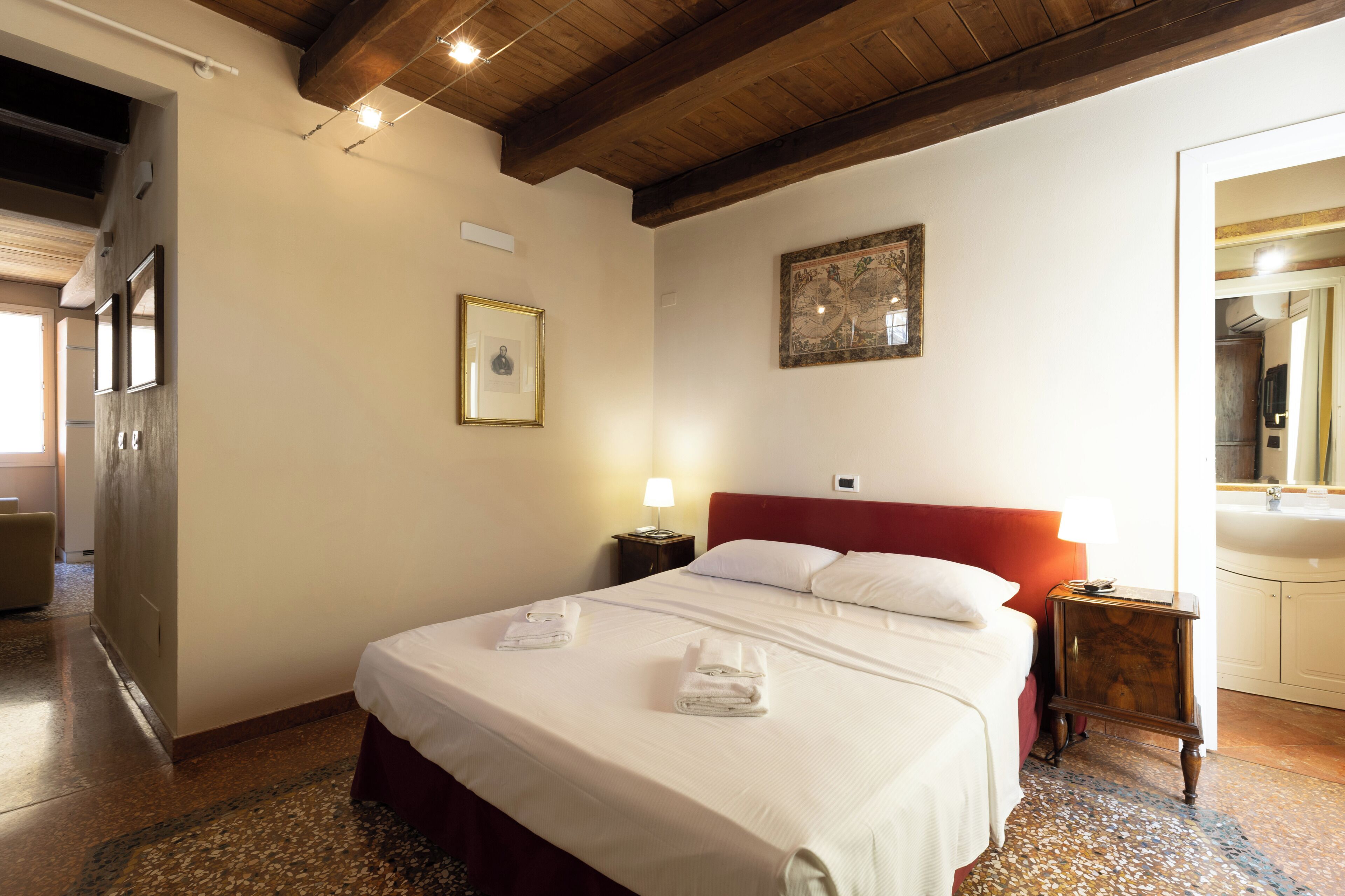 Habitación de hotel con una cama grande, techo de madera, un globo de pared y un baño visible a través de una puerta abierta.