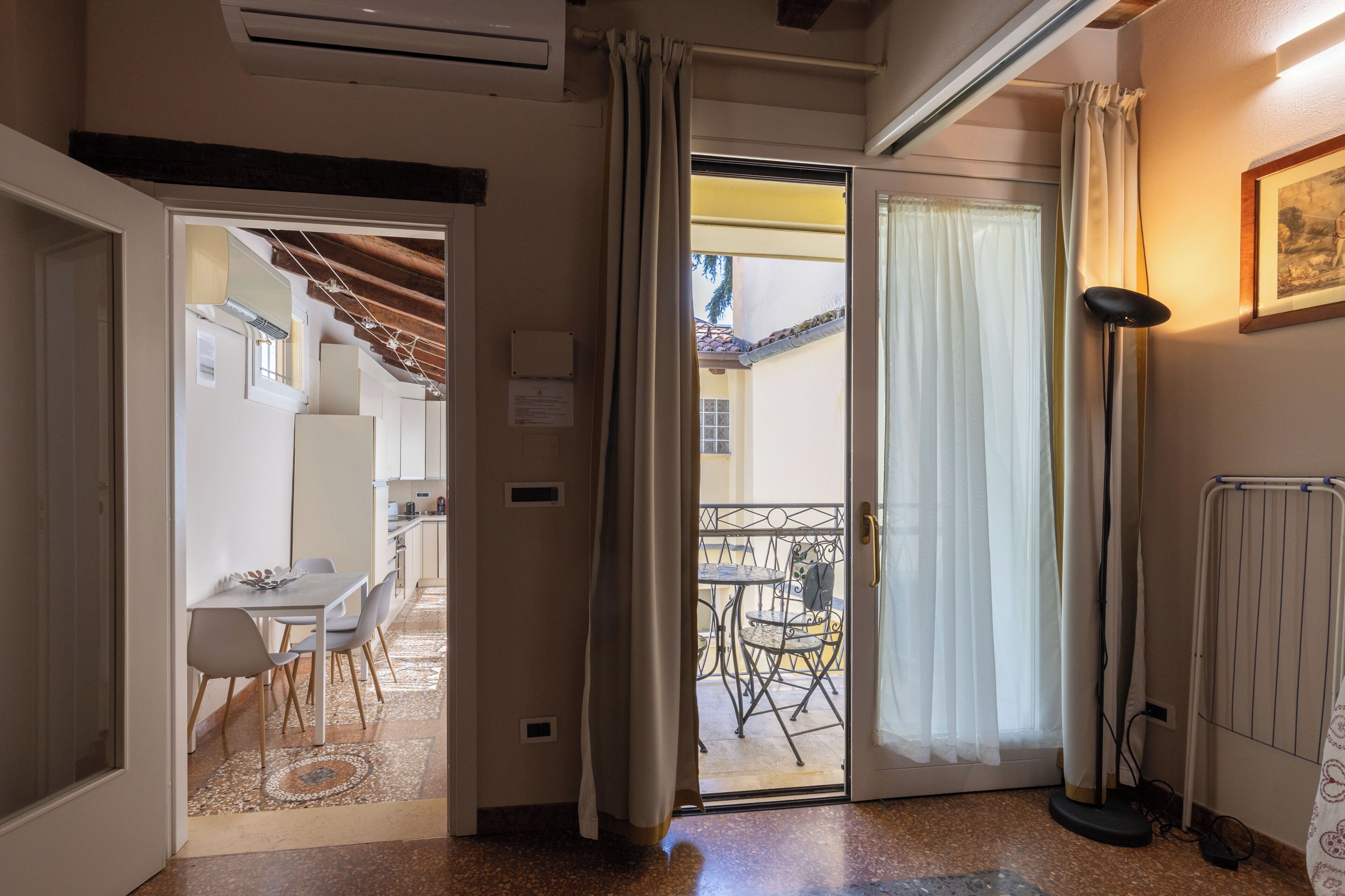 A hotel room with a dining area, a balcony with outdoor furniture, and a radiator on the wall.