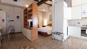 A compact hotel room with a kitchenette, a bed, a small dining area, and a bathroom.