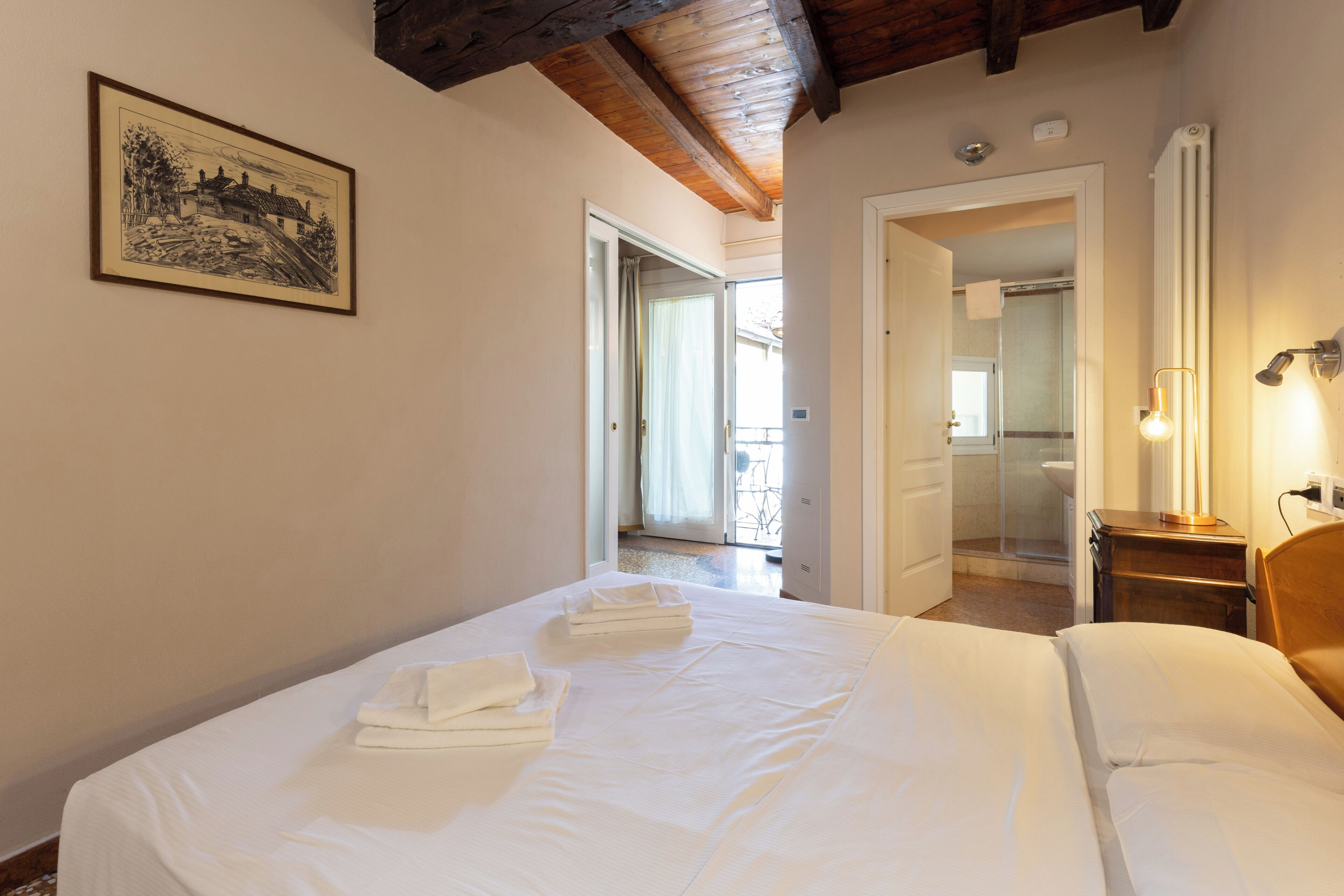 A hotel room with a bed, a bedside table, a lamp, and a framed picture on the wall.