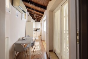A narrow hallway with a dining area featuring a table and chairs, a kitchen in the background, and a large sliding glass door leading to an outdoor area.