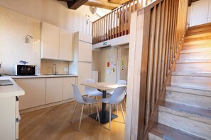 A modern kitchen with white cabinets, a wooden dining table with chairs, and a wooden staircase.