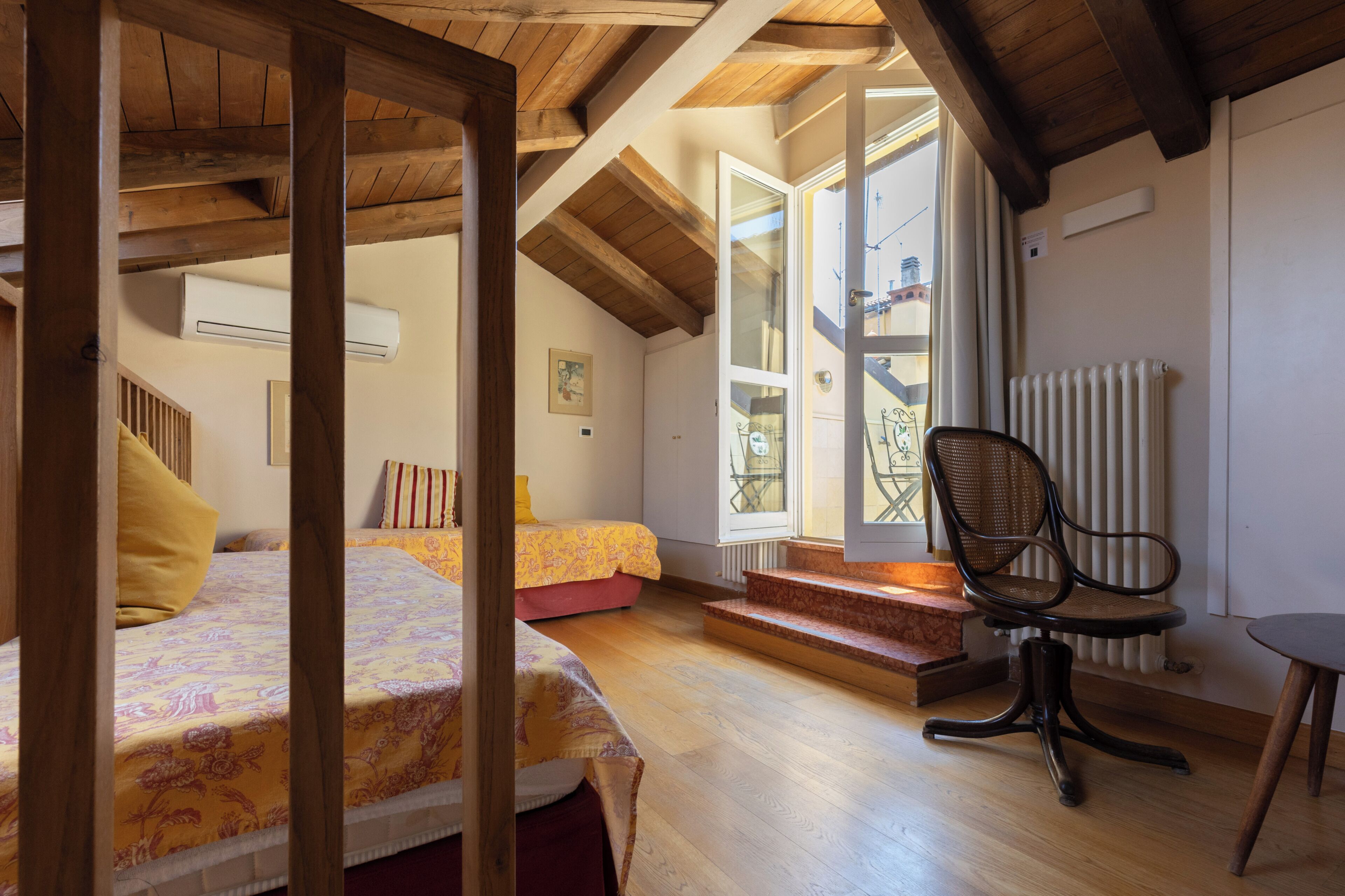 Un dormitorio con techo de madera, una cama con ropa de cama floral, una silla y un radiador.
