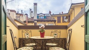 A small outdoor patio with a round table and four chairs, a potted plant, and a view of neighboring buildings.