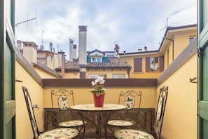 Un pequeño patio al aire libre con una mesa redonda y cuatro sillas, una planta en maceta y vistas de edificios vecinos.