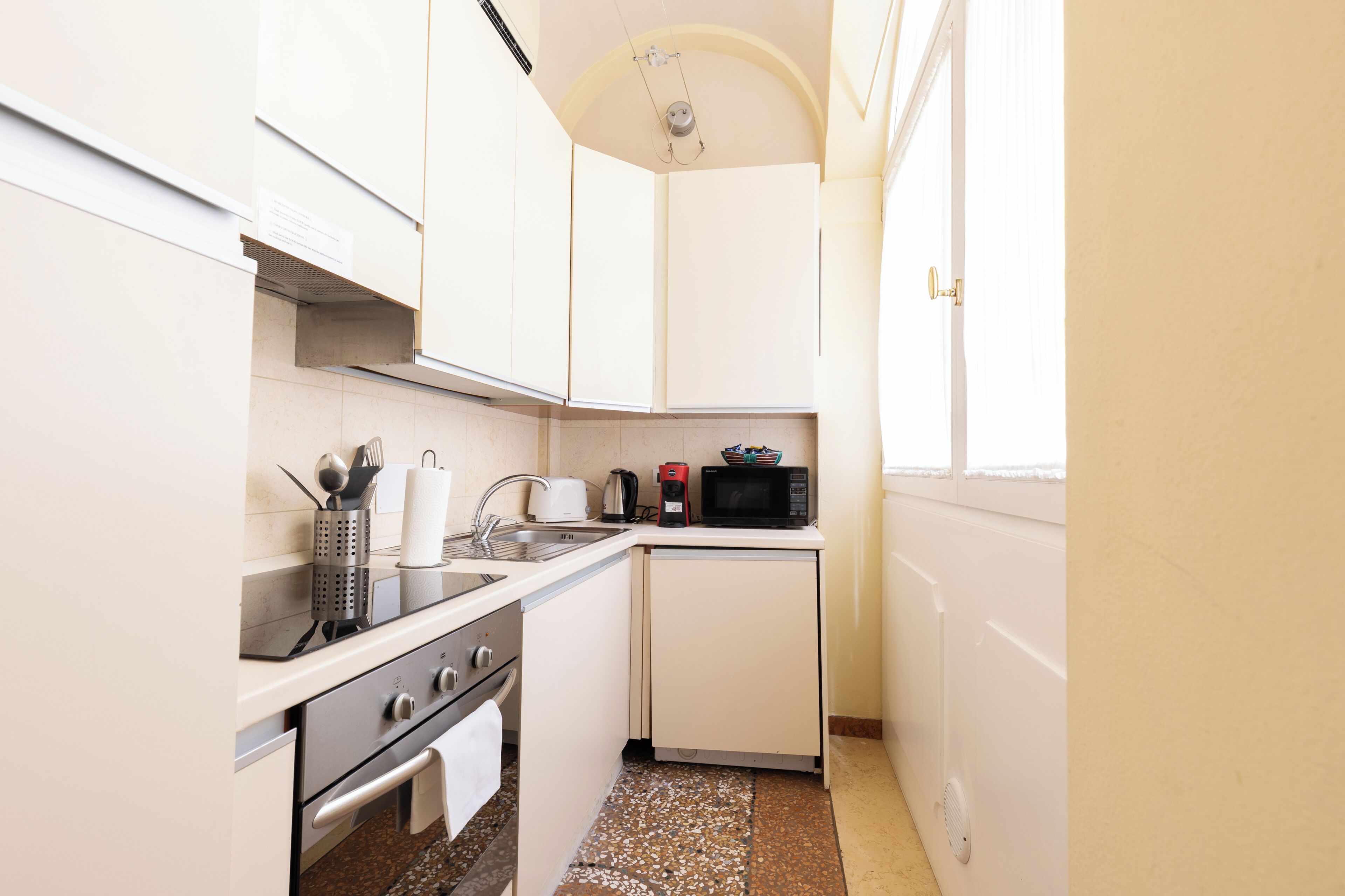 A compact kitchen with white cabinets, a sink, a stove, and a microwave.