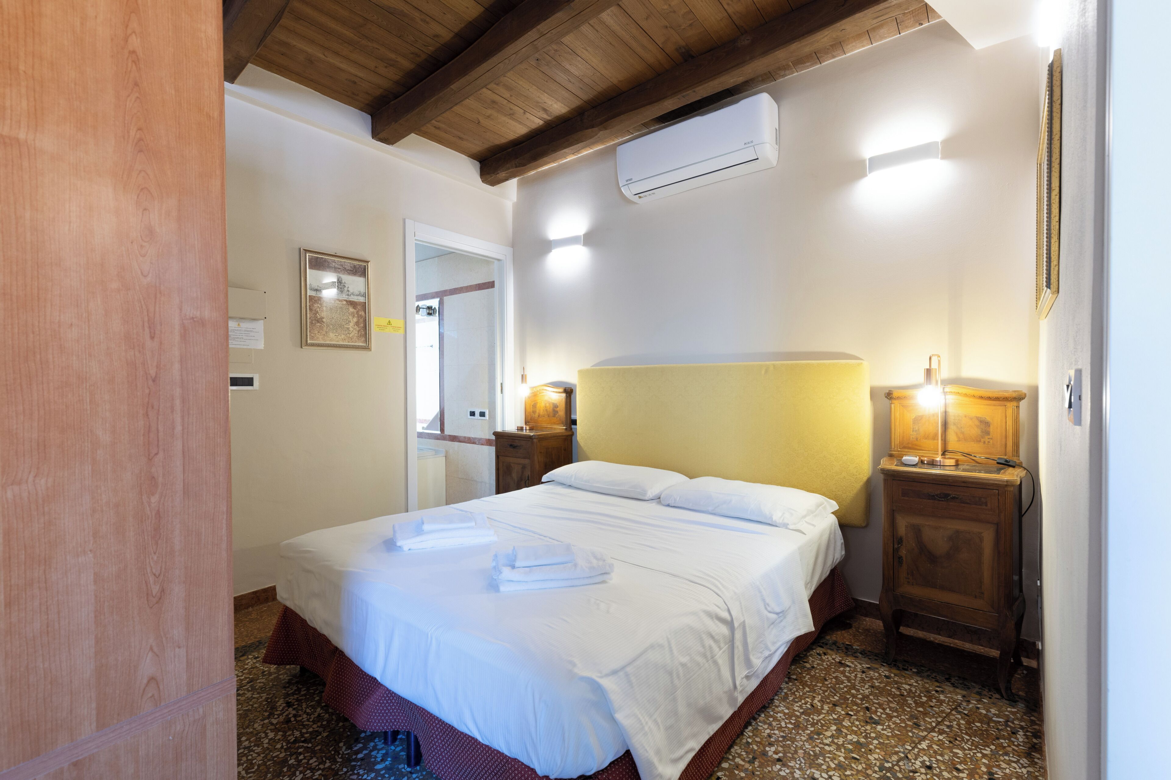 Ein Hotelzimmer mit Bett, Nachttischlampen, einer Klimaanlage und einer Holzbalkendecke.
