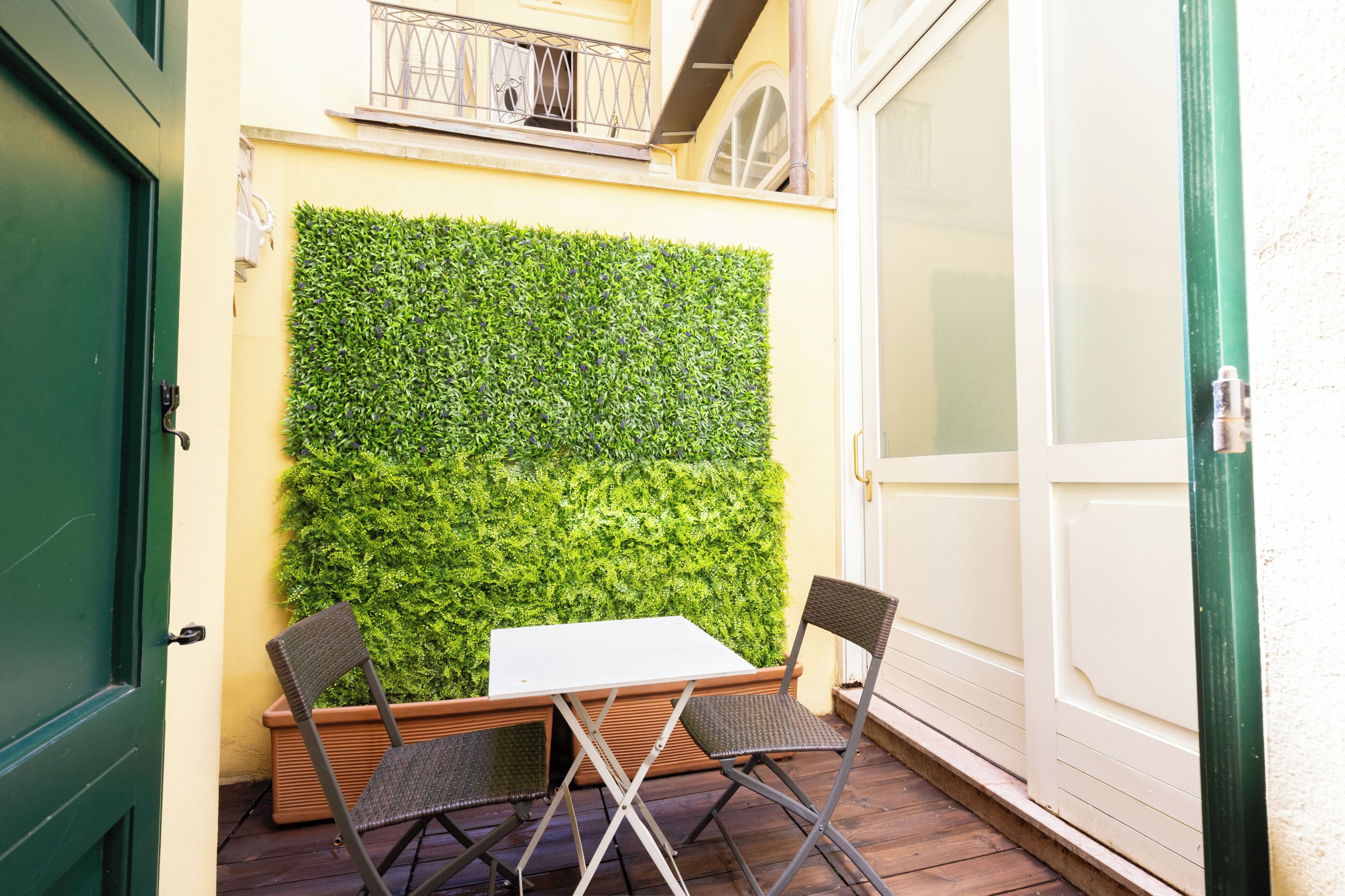 A patio with a table and two chairs, a green door, and a wall covered with green foliage.