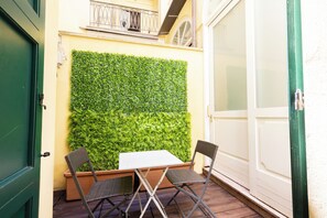A patio with a table and two chairs, a green door, and a wall covered with green foliage.