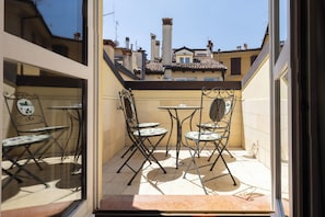 A small patio with two tables and four chairs, a window with a decorative mirror, and a view of neighboring buildings.
