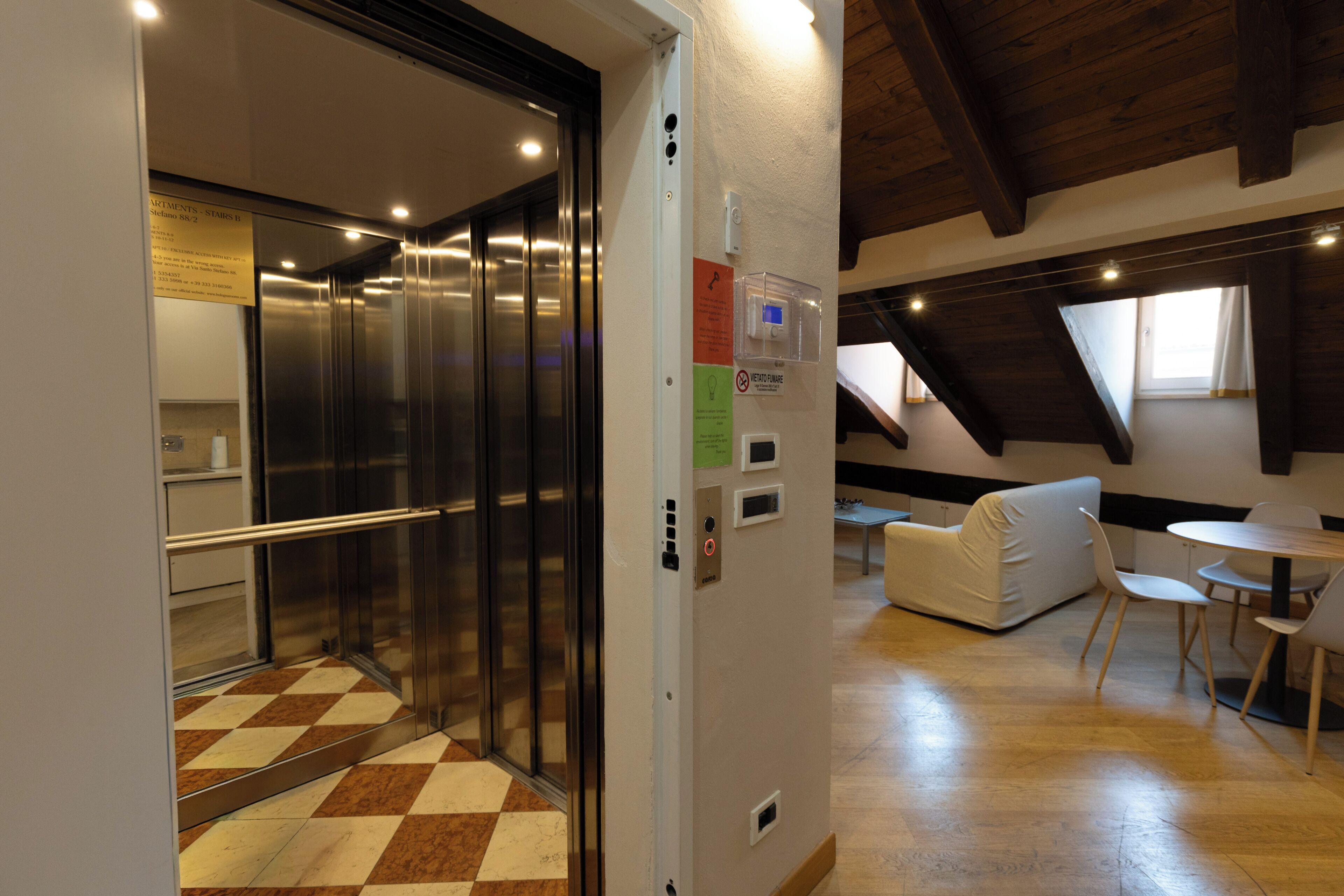 An elevator with a metallic finish, a wall-mounted intercom, and a check-in desk with a computer.