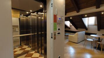 An elevator with a metallic finish, a wall-mounted intercom, and a check-in desk with a computer.