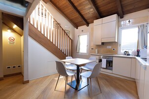 A modern kitchen with wooden flooring, a dining table with chairs, and a staircase with wooden railings.
