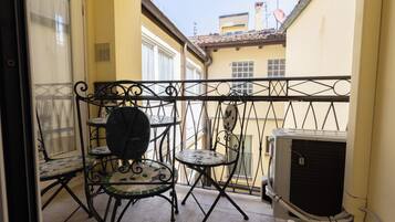 A balcony with a small table and chairs, an air conditioning unit, and a view of the street.