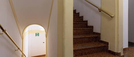 Un escalier avec une rampe, un sol à motifs et une porte portant un panneau indiquant la sortie de secours.