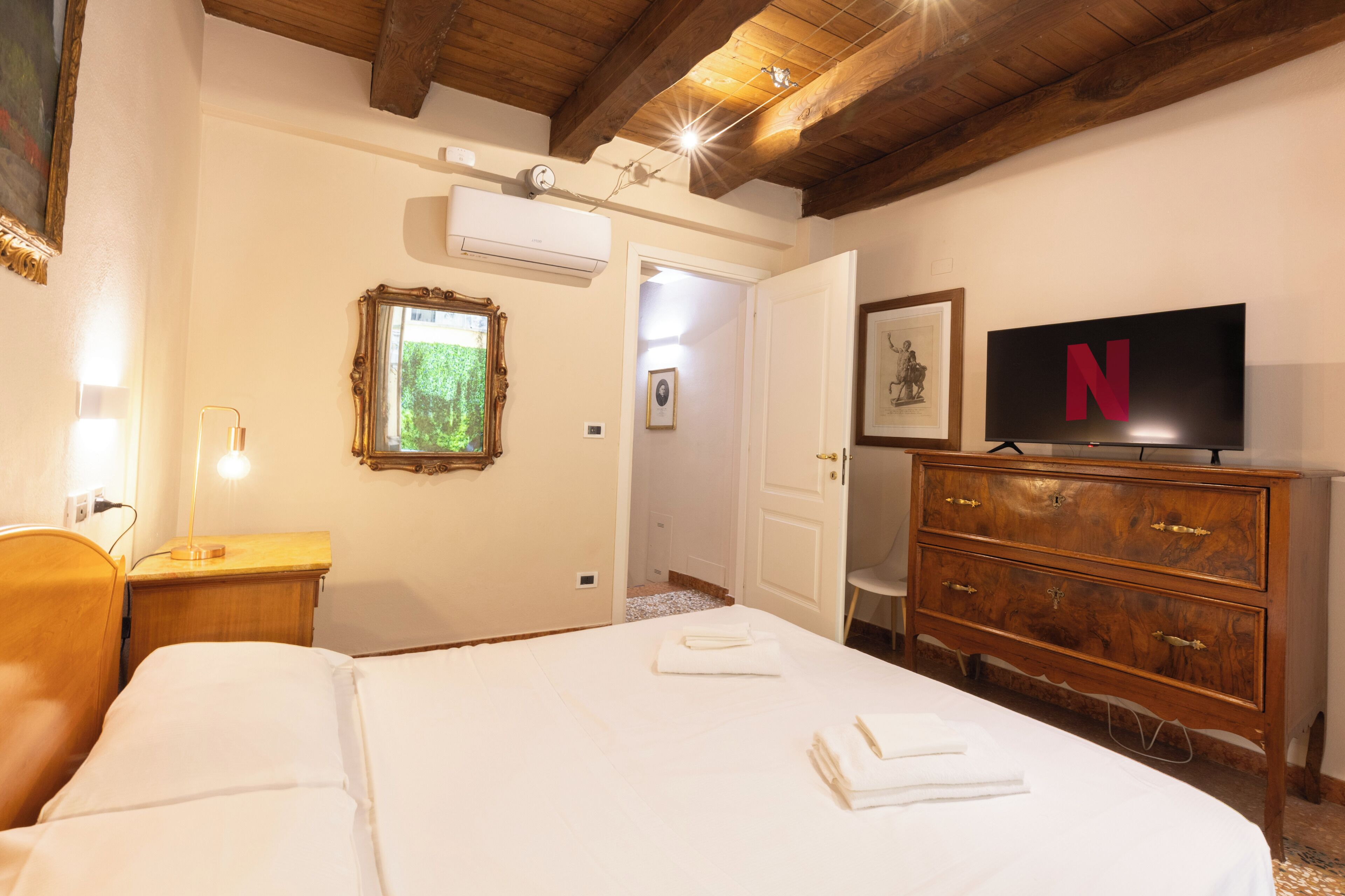 Ein Hotelzimmer mit einem Bett, einem Schminktisch, einem Fernseher und einer Tür zu einem weiteren Raum.