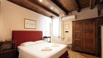 A hotel room with a large bed, a wooden wardrobe, a desk with a lamp, and a window with curtains.