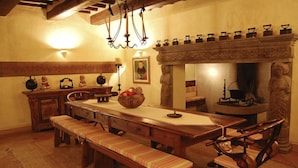 Ein traditioneller Speisesaal mit einem langen Holztisch, Bänken und einem Steinkamin.