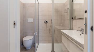 Un baño moderno con ducha de vidrio, inodoro y un lavabo grande con espejo.